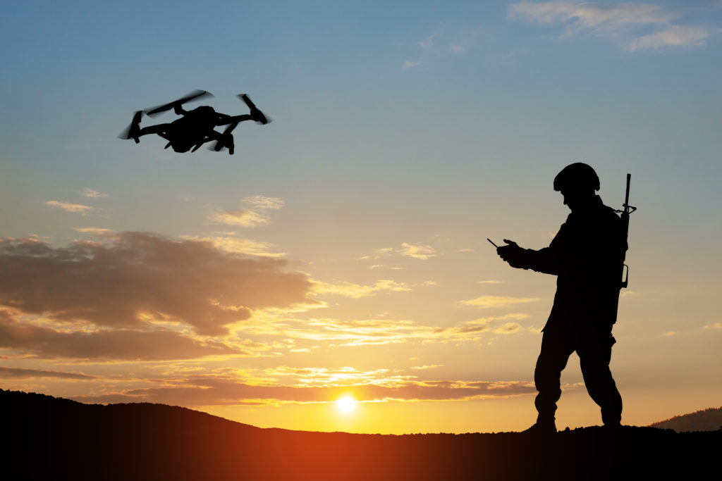 Silhouette of soldier using drone and laptop computer for scouting during military operation.