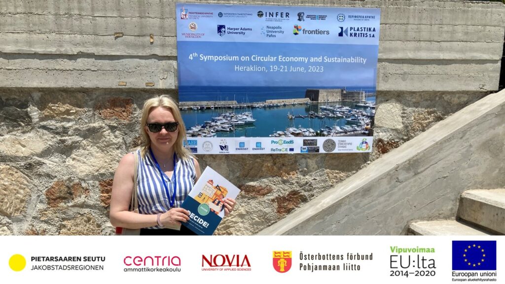 RDI-Specialist Mira Valkjärvi at the conference venue Cultural Conference Center of Heraklion Crete, holding the digital guide of the DeCiDe project. The picture includes logos of the funders of the DeCiDe project. Photo: Weimu You.