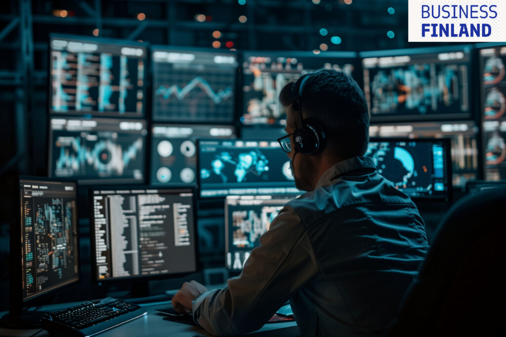 A man is sitting at a desk, typing on a keyboard. Behind the desk in the control room are numerous screens displaying various data and diagnostics.