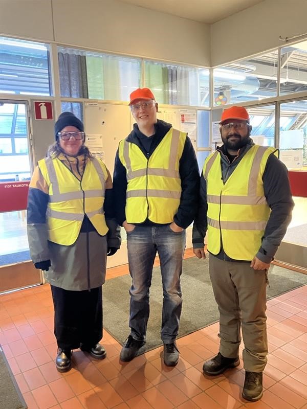 Three persons standing in protective clothing ready for a factory visit.