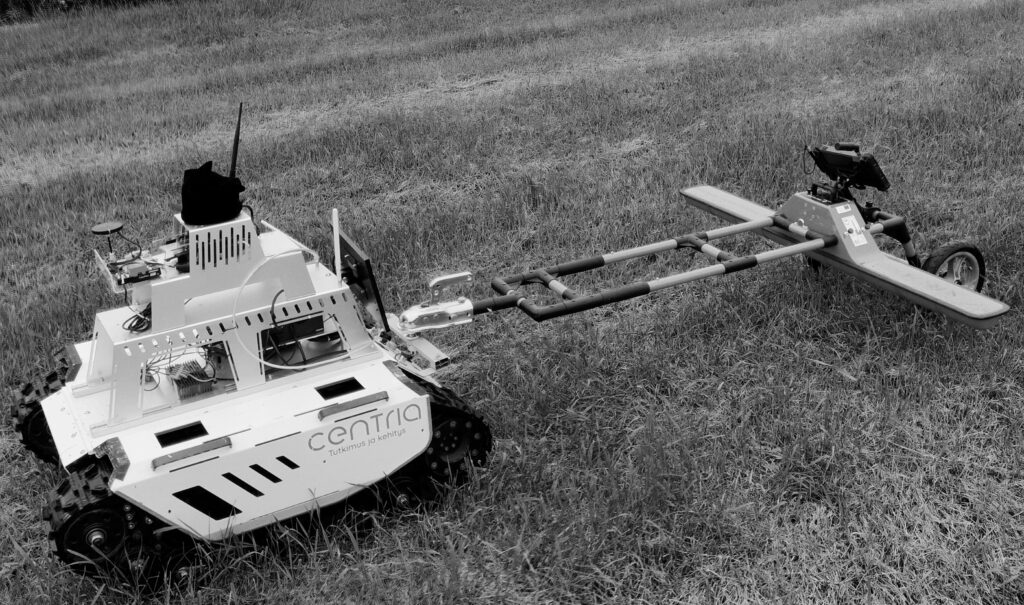 Miehittämätön maastoajoneuvo (UGV) liikkuu tutkimusalueella ja vetää perässään maatutka-antennia, jolla kerätään tietoa maaperän rakenteista.