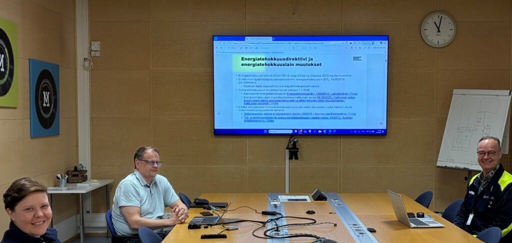 Kuvassa ihmisiä ja iso näyttö kokoushuoneessa.